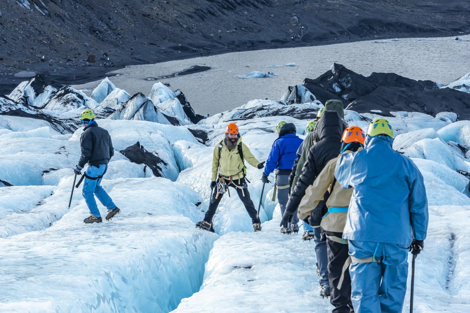 Guide assists people over a crack in a glacier