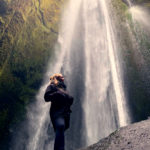 A woman is standing in front of a waterfall.