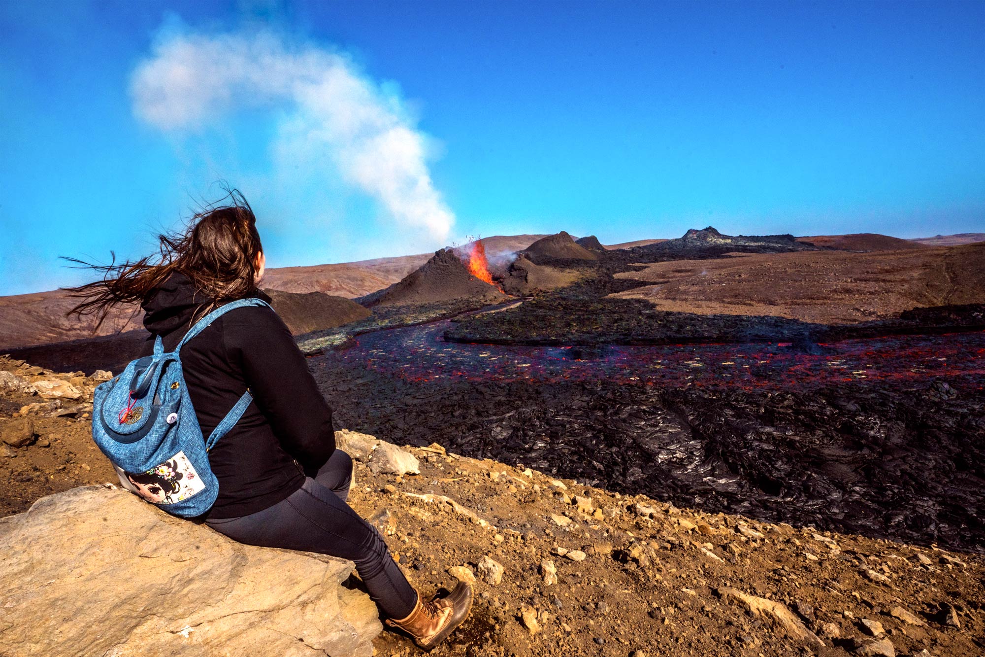 Girl sitting and watching an active volcano eruption
