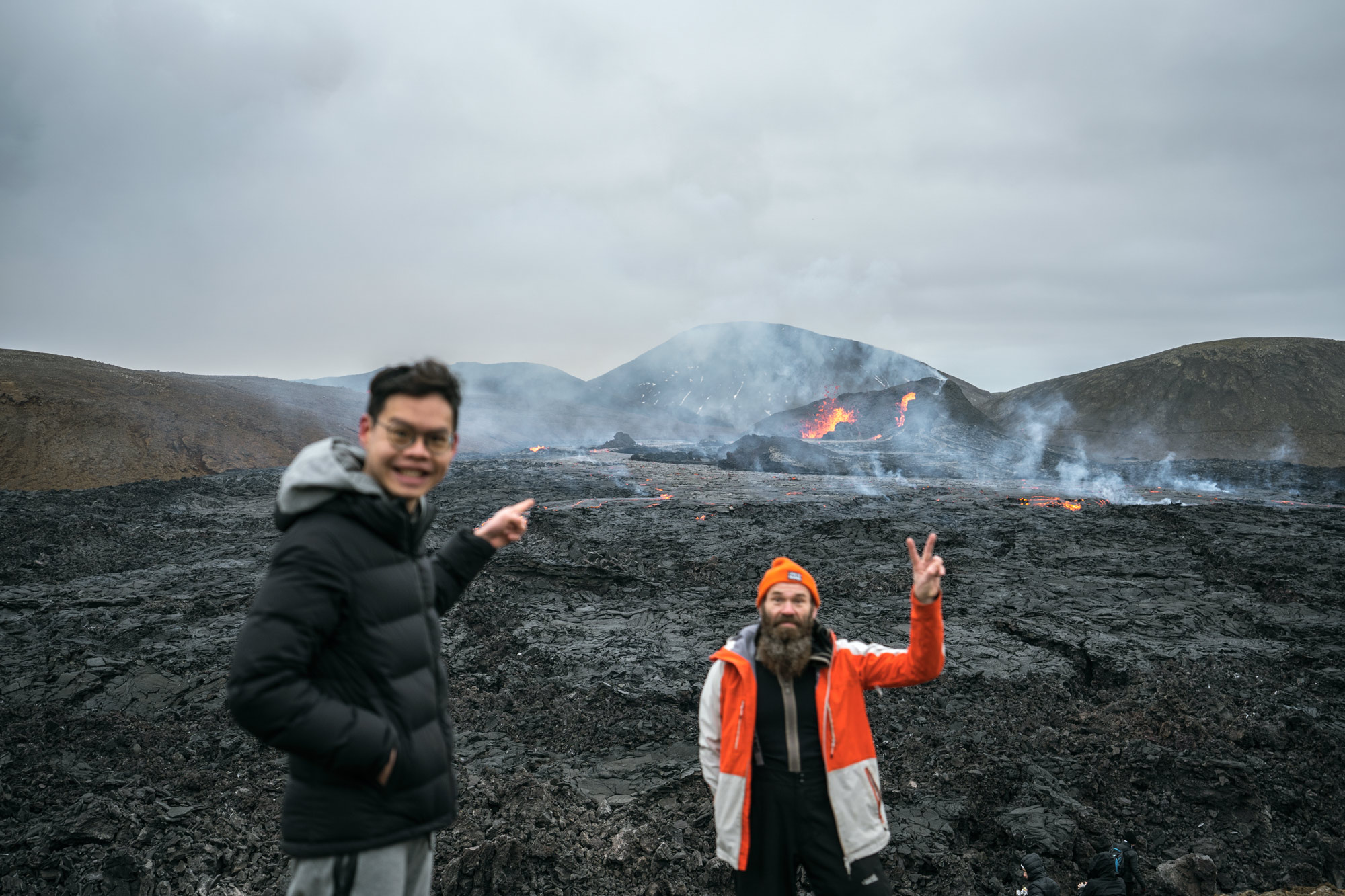 Two men in front of the new lava. Blowing craters in behind.
