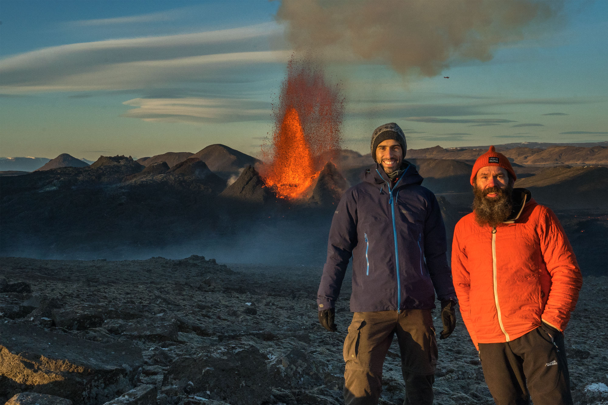Two men standing in front of active volcano
