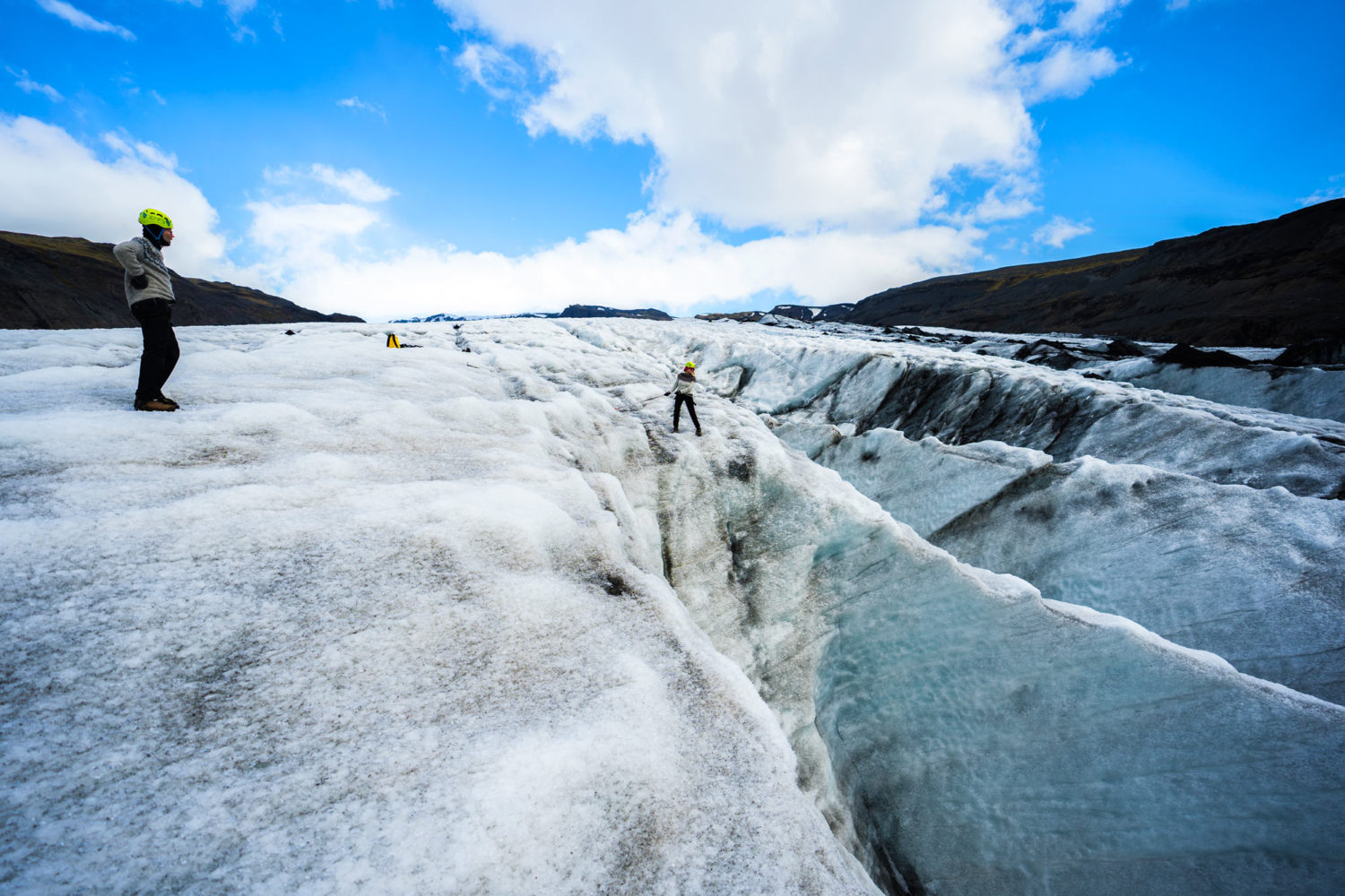 A woman stands on the edge of a glacier looking down.