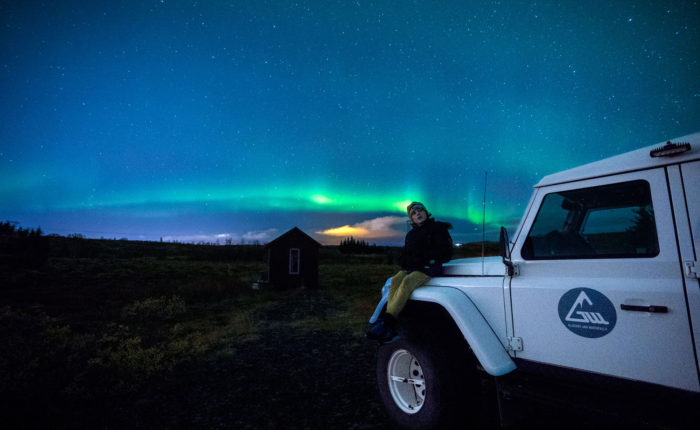A boy sitting on a Defender looking at Northern Lights
