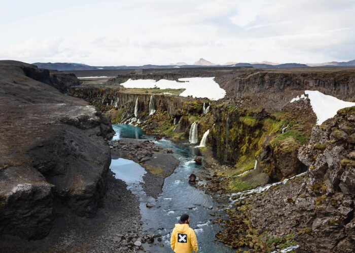 A man standing in front of Icelandic canyon with many small waterfalls