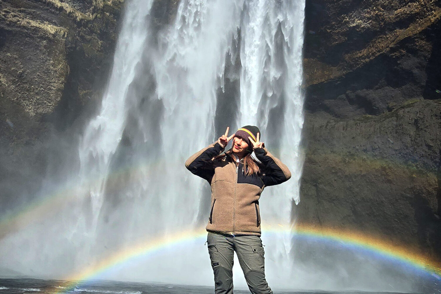 A woman staning in front of a waterfall and a rainbow