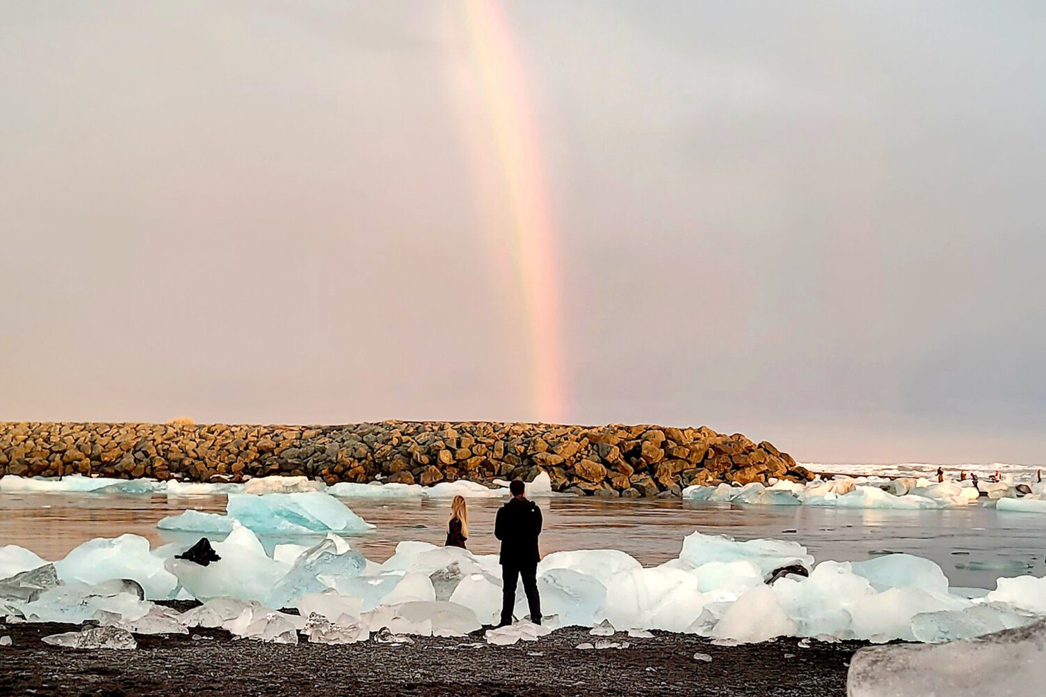 People on the black diamond beach taking photo of the ice bergs and the rainbow.