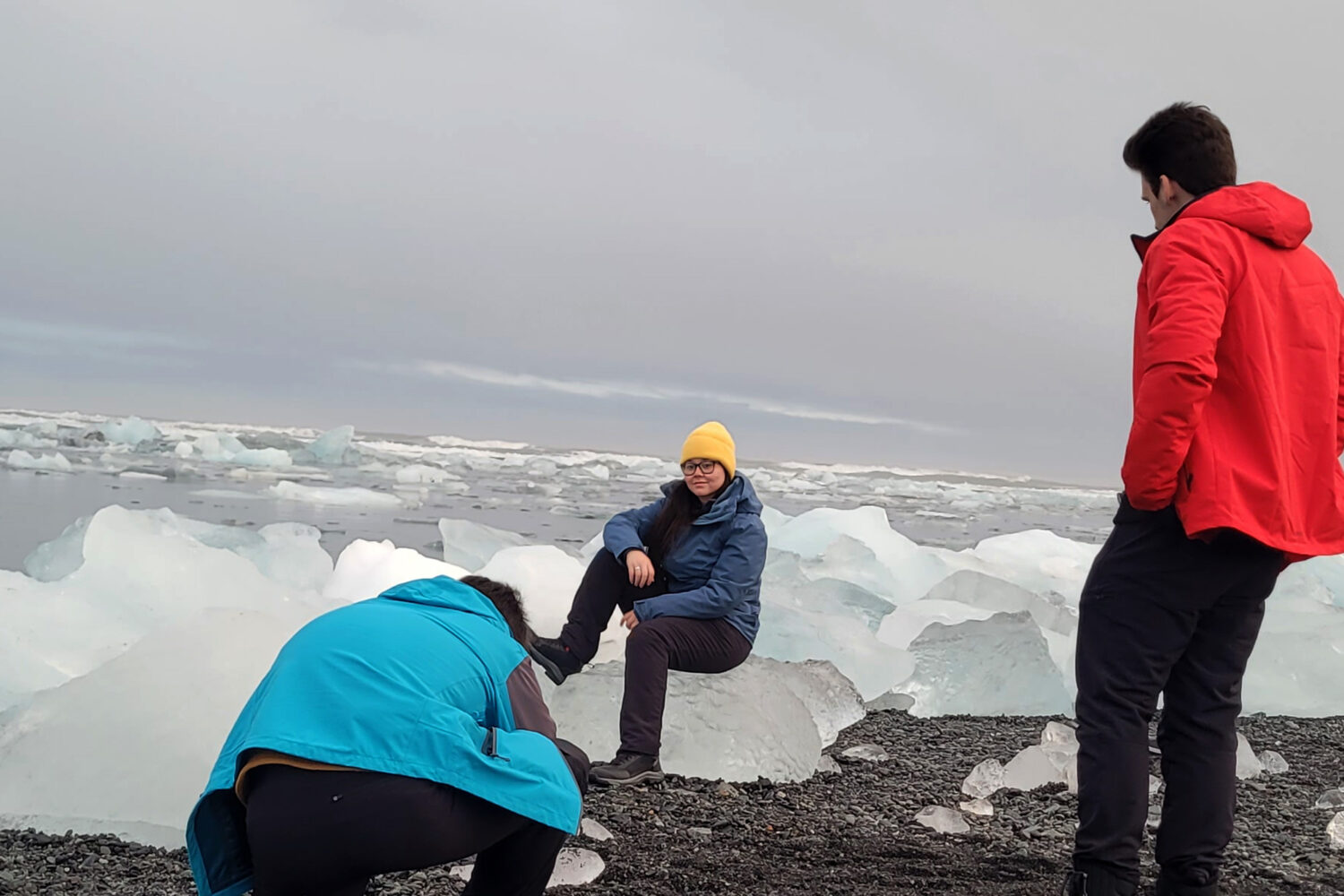 A girl sitting on an ice berg on the Black Diamond Beach and a man in front working on the camera.