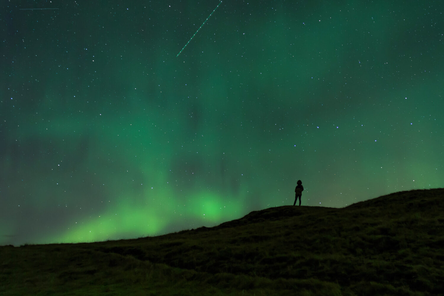 Silhouette of a person beneath the swirling Northern Lights