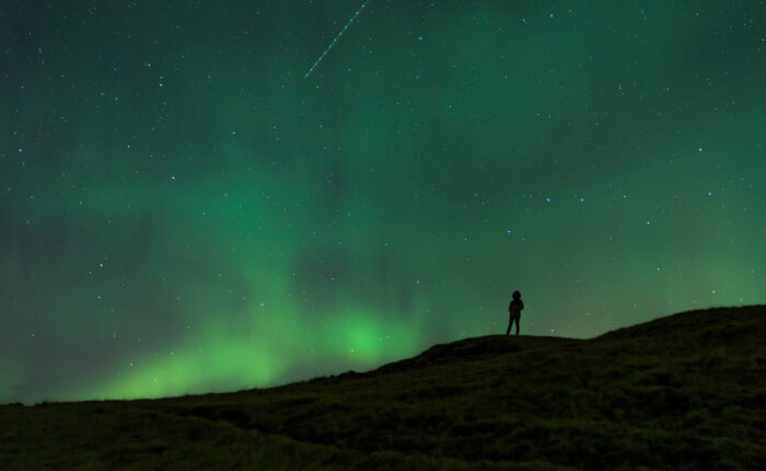 Silhouette of a person beneath the swirling Northern Lights