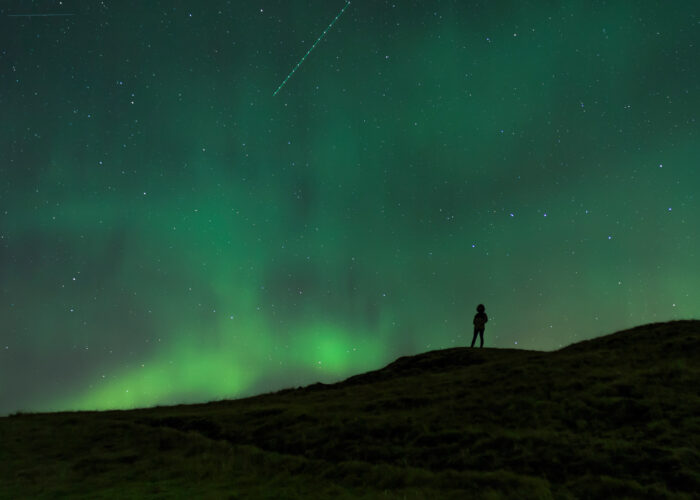 Silhouette of a person beneath the swirling Northern Lights