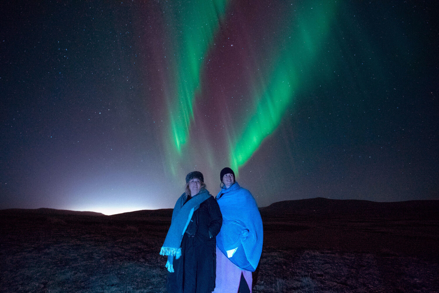 Mother and daughter standing in front the Northern Lights, dancing across the night sky, offer a breathtaking spectacle of nature's beauty.