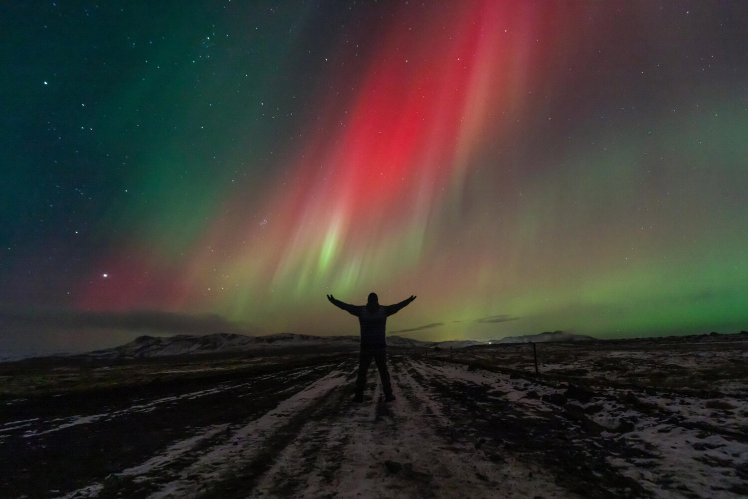 A man standing in front the Northern Lights, in all their glorious colors, dancing across the night sky in shades of green, pink, purple, and red, offer a breathtaking spectacle of nature's beauty.